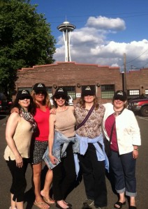 Standing in front of the Seattle Space Needle (trust us), wearing their Souvenir Village hats are, from left to right: Heather Pearse Soto, Sophia Sims Shannon, Laray Lawson Van slyke, Rena Hudon Hryckewicz, and Dawn Ward Lenci