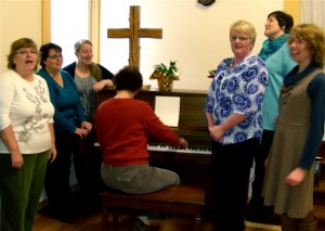 Singing for their Supper: Cindy Rose, Dee Kraft, Karla Dalious, Marie Adams (on piano), Donna Dutton, Mary Brophy-Moore, Amy Bartel. Courtesy photo